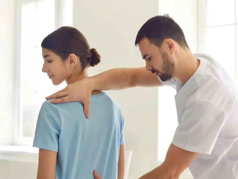 Physical therapist assessing a seated patient's back and shoulder